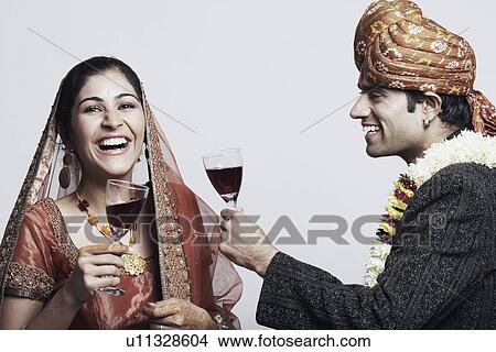 Picture - Side profile of a newlywed couple holding glasses of red wine. Fotosearch