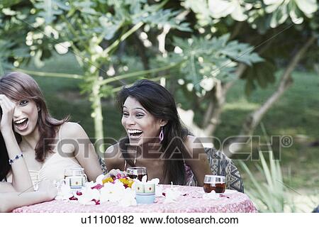 Two young women sitting at a table and laughing View Large Photo Image Stock Image - Two young women sitting at a table and laughing. Fotosearch