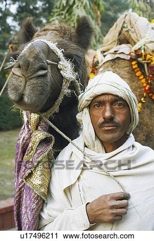 Stock Image - Portrait of a mid adult man standing with a camel. Fotosearch
