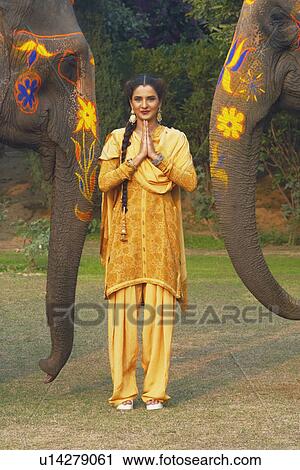 Stock Image - Portrait of a young woman greeting in front of two elephants. Fotosearch