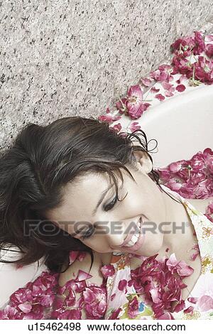 Stock Photo - High angle view of a young woman lying in a bathtub covered with flower petals. Fotosearch