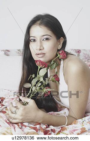 Portrait of a young woman lying on the bed holding roses View Large Photo Image Stock Photograph - Portrait of a young woman lying on the bed holding roses. Fotosearch