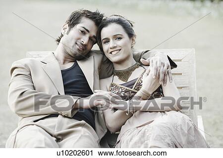 Stock Image - Portrait of a young couple sitting on a bench. Fotosearch