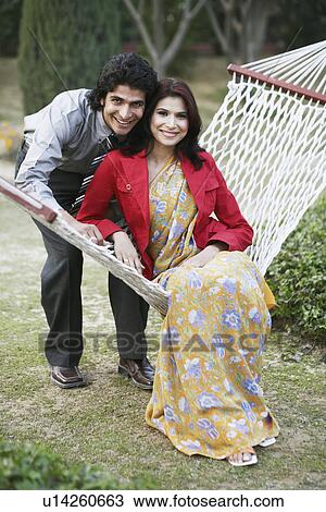 Stock Image - Portrait of a young man bending over a young woman sitting in a hammock. Fotosearch