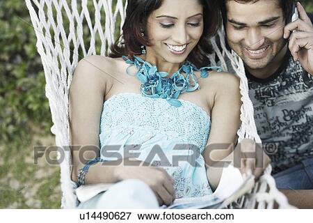 Young couple looking at a magazine View Large Photo Image Stock Photo - Young couple looking at a magazine. Fotosearch