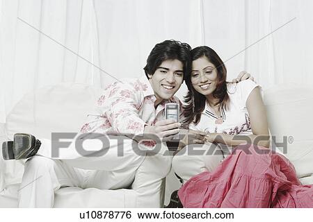 Young couple looking at a mobile phone View Large Photo Image Stock Photograph - Young couple looking at a mobile phone. Fotosearch