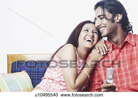 Stock Image - Young couple sitting on a couch smiling. Fotosearch