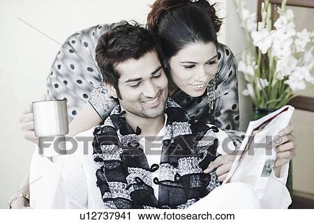Stock Image - Young woman bending over a young man reading a magazine. Fotosearch