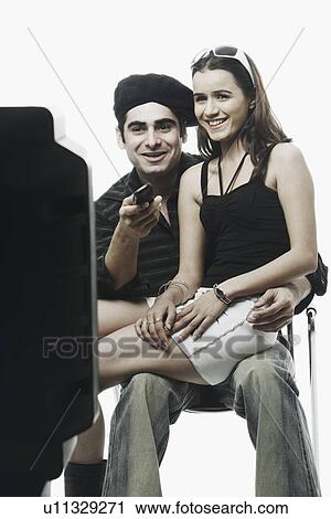 Stock Image - Young woman sitting on a young man's lap watching television. Fotosearch