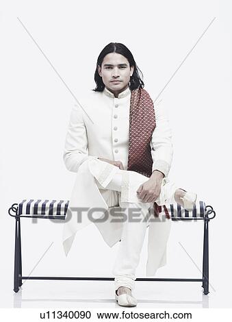 Stock Image - Portrait of a young man in traditional clothing sitting on a bench. Fotosearch