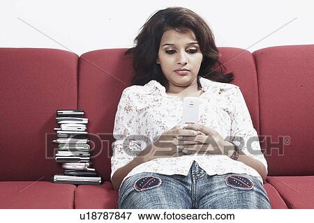 Stock Photo - Close-up of a young woman sitting on a couch operating a mobile phone. Fotosearch