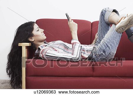 Side profile of a young woman lying on the couch operating a mobile phone View Large Photo Image Stock Image - Side profile of a young woman lying on the couch operating a mobile phone. Fotosearch