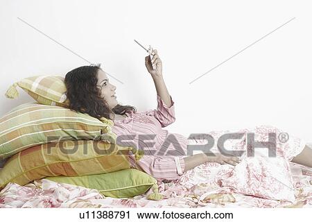 Stock Image - Side profile of a young woman lying down and using a mobile phone. Fotosearch