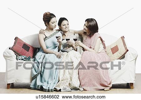 Stock Image - Close-up of three young women sitting on a couch holding wineglasses. Fotosearch