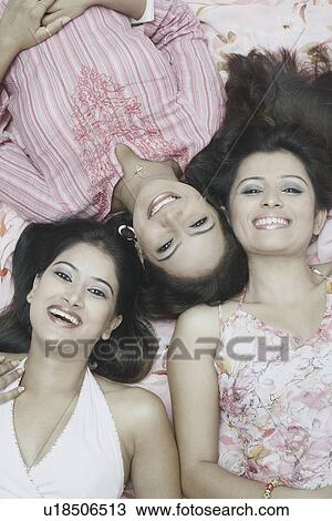 Stock Image - High angle view of three young women lying down and smiling. Fotosearch