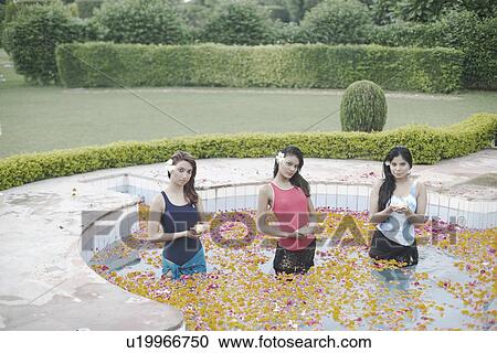 Stock Image - Portrait of three young women holding candles and standing in a swimming pool. Fotosearch