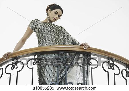Stock Photography - Low angle view of a young woman standing in the balcony. Fotosearch