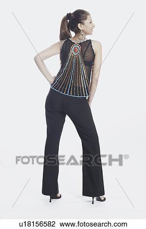 Stock Image - Rear view of a young woman with arms akimbo. Fotosearch