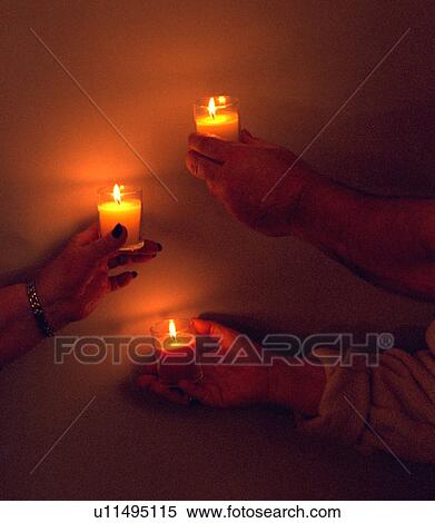Stock Photography - Three hands holding lighted candles. Fotosearch