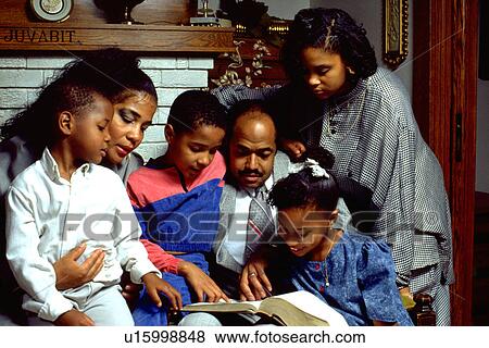 Stock Photo - African American family reading Bible in their home with children and parents. Fotosearch