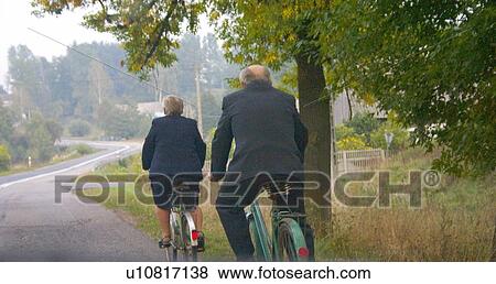 Stock Photo - Well dressed older couple riding bicycles along road. Fotosearch