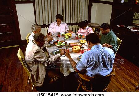 Stock Photography - Family of three generations saying grace at dinner table. Fotosearch