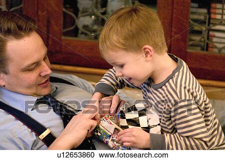 Stock Image - Son helping dad age 4 and 34 open his birthday gift. Fotosearch