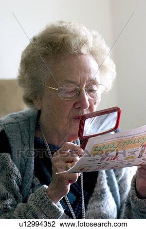 Stock Image - Senior reading ad with magnifying lens. Fotosearch
