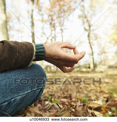 Stock Image - Caucasian man sitting on ground meditating in rural setting.. Fotosearch