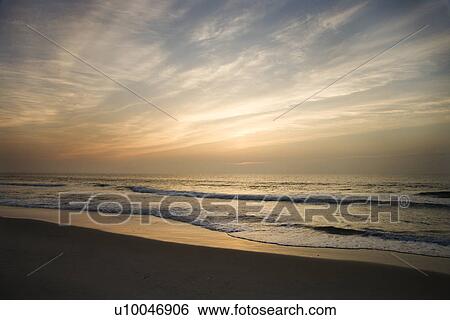 Stock Photograph - Ocean waves lapping on the shore at sunset.. Fotosearch