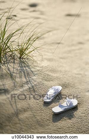 Stock Image - Two white sandals on sandy beach.. Fotosearch