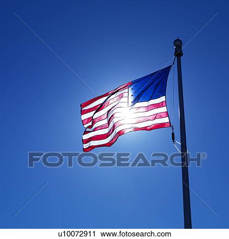 American flag on flagpole waving against blue sky with sun shining through from behind. View Large Photo Image Stock Image - American flag on flagpole waving against blue sky with sun shining through from behind.. Fotosearch