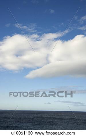 Stock Image - Blue sky with fluffy white clouds over ocean horizen.. Fotosearch
