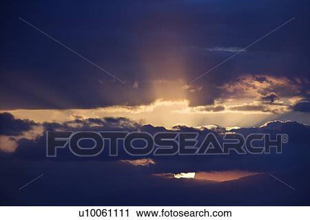Stock Image - Sunbeams coming through clouds at sunrise over Maui, Hawaii, USA.. Fotosearch