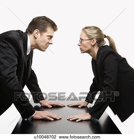 Stock Image - Caucasian mid-adult businessman and woman staring at each other with hostile expressions.. Fotosearch