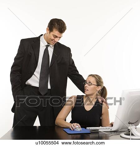 Caucasian mid-adult man touching shoulder of woman sitting at computer who feels uncomfortable. View Large Photo Image Picture - Caucasian mid-adult man touching shoulder of woman sitting at computer who feels uncomfortable.. Fotosearch