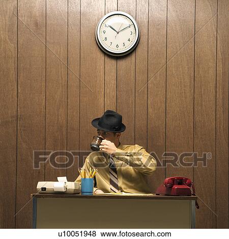 Caucasion mid-adult retro businessman wearing fedora sitting at desk drinking coffee. View Large Photo Image Stock Photo - Caucasion mid-adult retro businessman wearing fedora sitting at desk drinking coffee.. Fotosearch