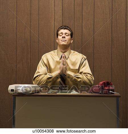 Stock Photo - Caucasion mid-adult retro businessman sitting at desk praying in gratitude.. Fotosearch