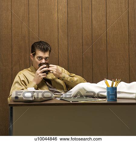 Stock Photograph - Caucasion mid-adult retro businessman sitting with feet propped on desk drinking coffee.. Fotosearch