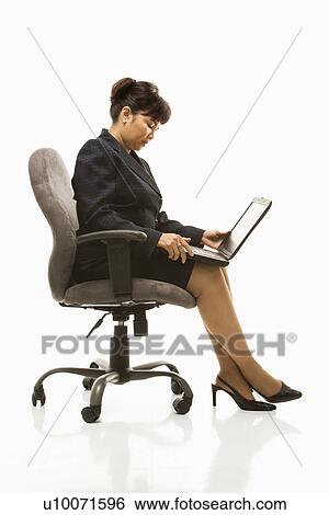 Stock Photograph - Filipino middle-aged businesswoman sitting in office chair with laptop against white background.. Fotosearch