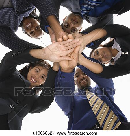Stock Photo - Low angle portrait of multi-ethnic business group of men and women with hands in huddle.. Fotosearch
