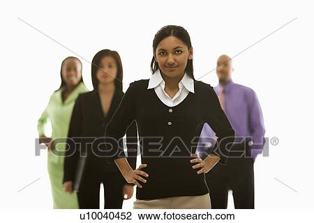 Stock Image - Portrait of Indian businesswoman smiling with hands on hips with others in background.. Fotosearch