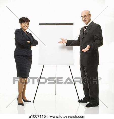 Smiling Caucasian middle-aged businessman and Filipino businesswoman standing making presentation against white background. View Large Photo Image Picture - Smiling Caucasian middle-aged businessman and Filipino businesswoman standing making presentation against white background.. Fotosearch