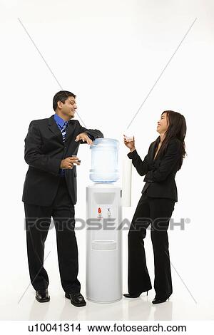 Vietnamese businesswoman and Indian businessman conversing at water cooler. View Large Photo Image Picture - Vietnamese businesswoman and Indian businessman conversing at water cooler.. Fotosearch