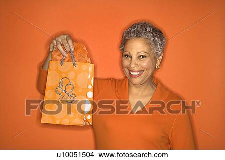 Picture - African American mature adult female holding gift bag.. Fotosearch