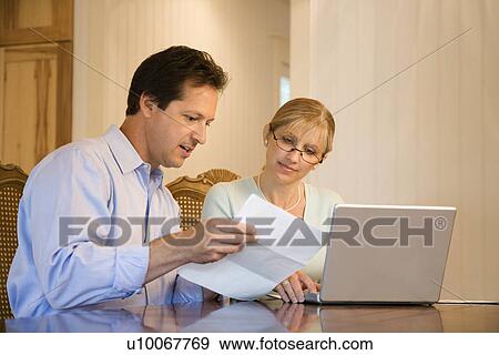 Stock Photo - Caucasian mid-adult couple paying bills on laptop computer.. Fotosearch