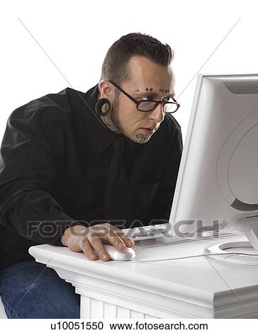 Stock Image - Caucasian mid-adult man with tattoos and piercings using computer.. Fotosearch