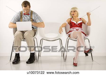 Stock Image - Caucasian young man dressed like nerd sitting with laptop with Caucasian young blonde woman looking at him.. Fotosearch
