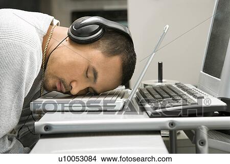 Close-up of Asian young adult man sleeping with head on laptop keyboard and wearing headphones. View Large Photo Image Picture - Close-up of Asian young adult man sleeping with head on laptop keyboard and wearing headphones.. Fotosearch