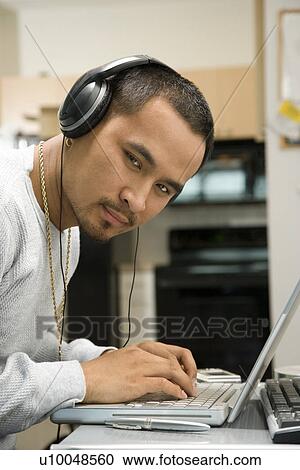 Close-up of Asian young adult man wearing headphones working on laptop and looking at viewer. View Large Photo Image Stock Image - Close-up of Asian young adult man wearing headphones working on laptop and looking at viewer.. Fotosearch